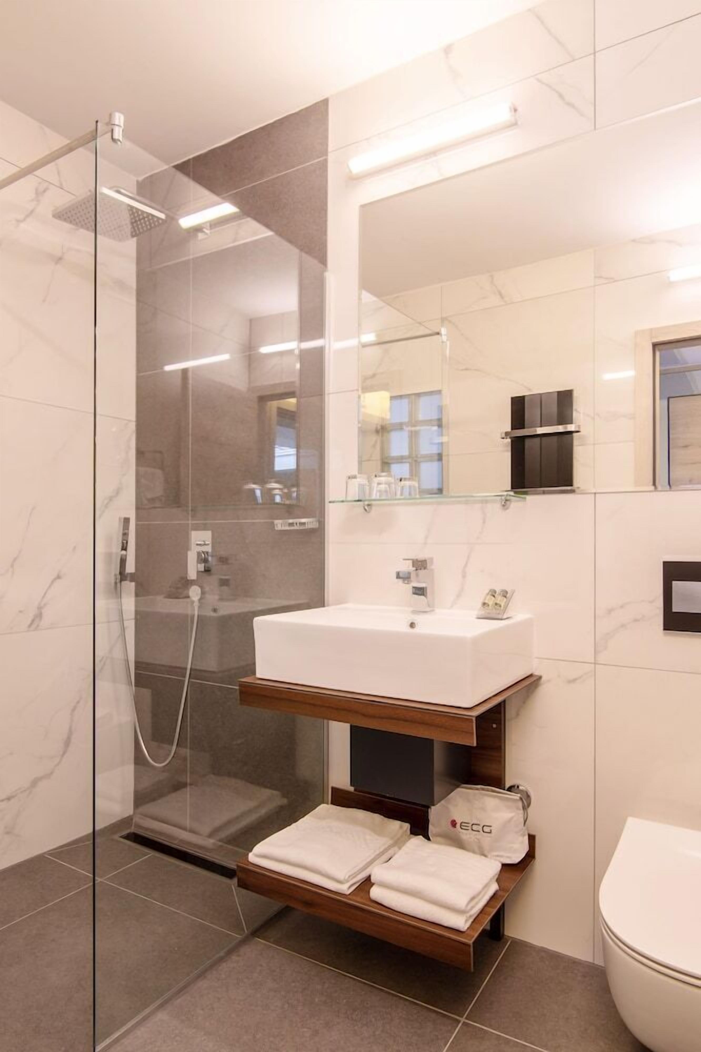 A modern bathroom with a glass-enclosed shower, a white sink, and a wooden vanity.