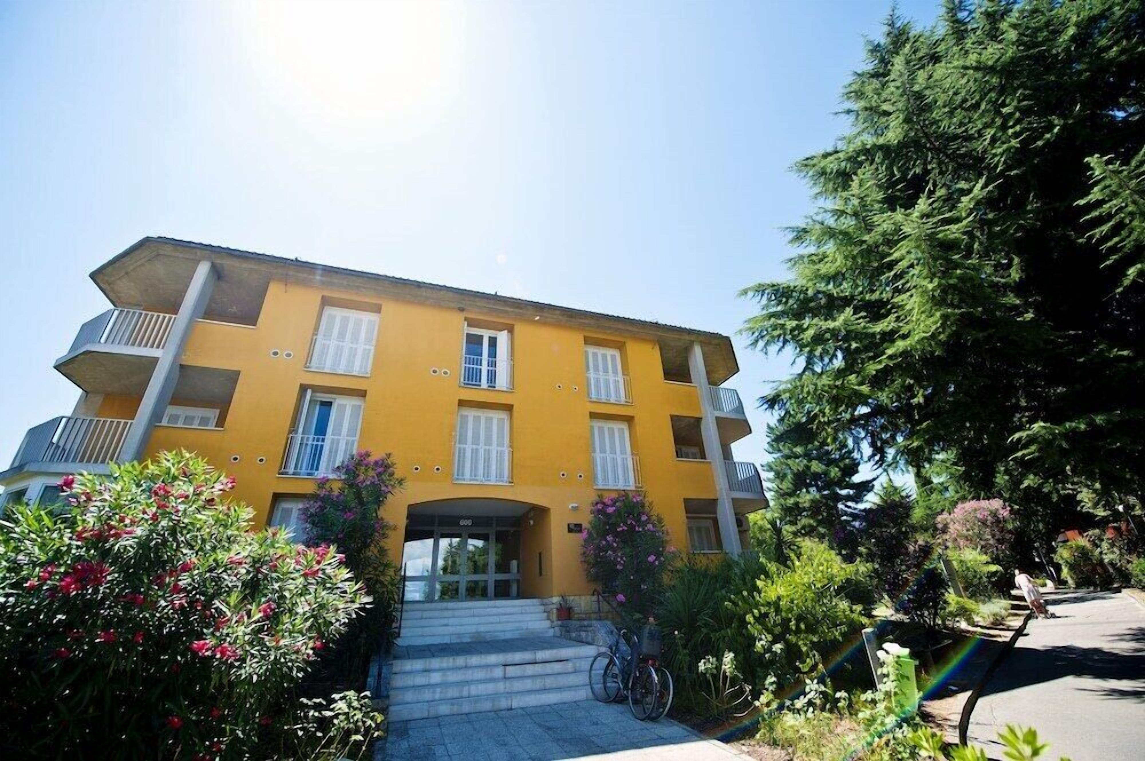 Un edificio giallo a più piani con balconi, una bicicletta parcheggiata di fronte e un cielo sereno.
