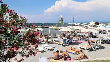 A beach with sun loungers and umbrellas, a lifeguard tower, and a clear view of the sea.