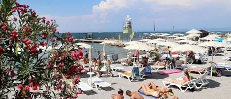 A beach with sun loungers and umbrellas, a lifeguard tower, and a clear view of the sea.
