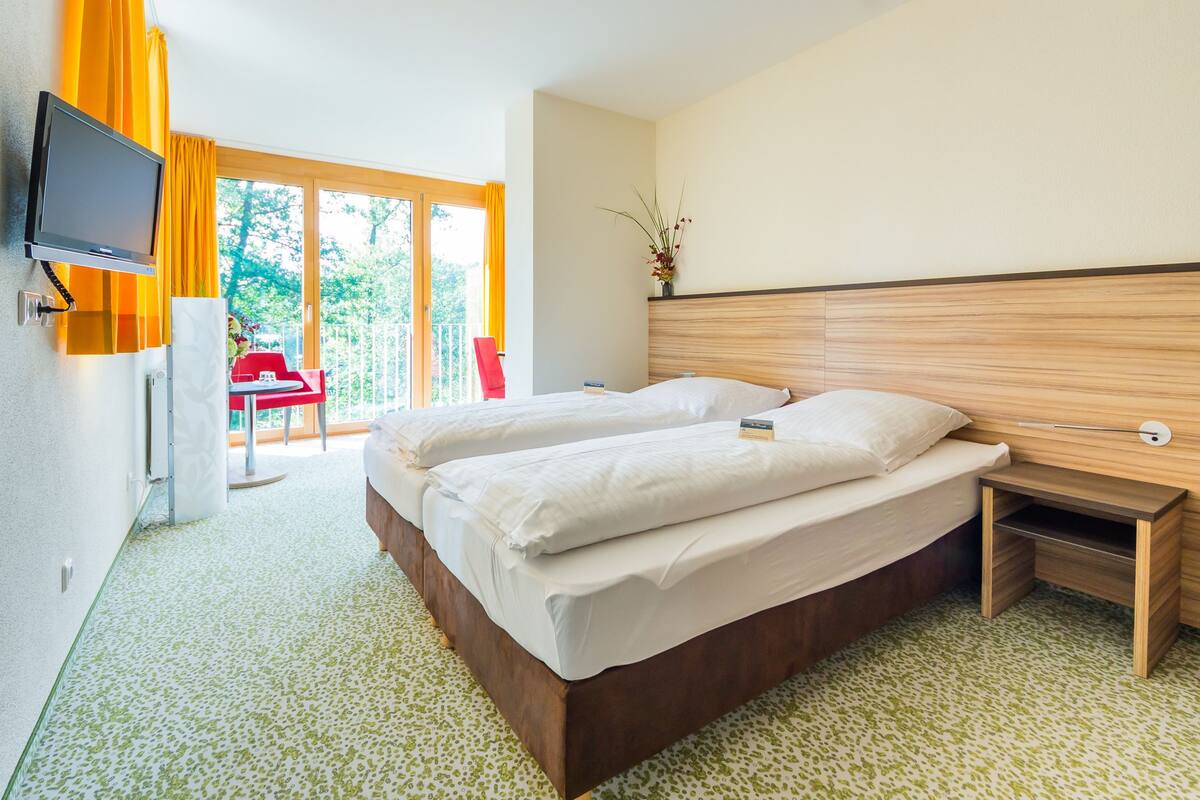 Une chambre d’hôtel avec un grand lit, un téléviseur fixé au mur et une petite table placée à côté du lit.