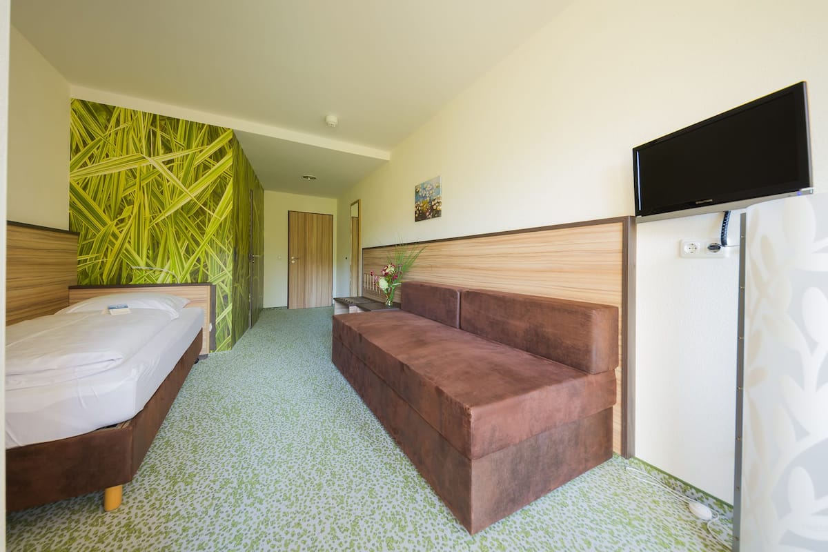 Une chambre d’hôtel avec un lit, un canapé, une télévision et un mur orné d’un motif de feuilles vertes.