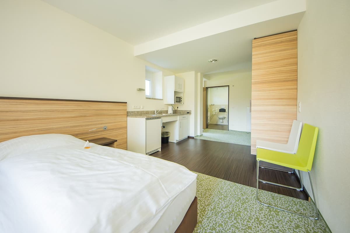 Une chambre d’hôtel comprenant un lit, un petit bureau, une chaise, une kitchenette et une salle de bain.