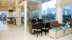 A modern hotel lobby with glass walls, a reception desk, seating area, and a view of the outside. - Princess Hotel (Da Nang)
