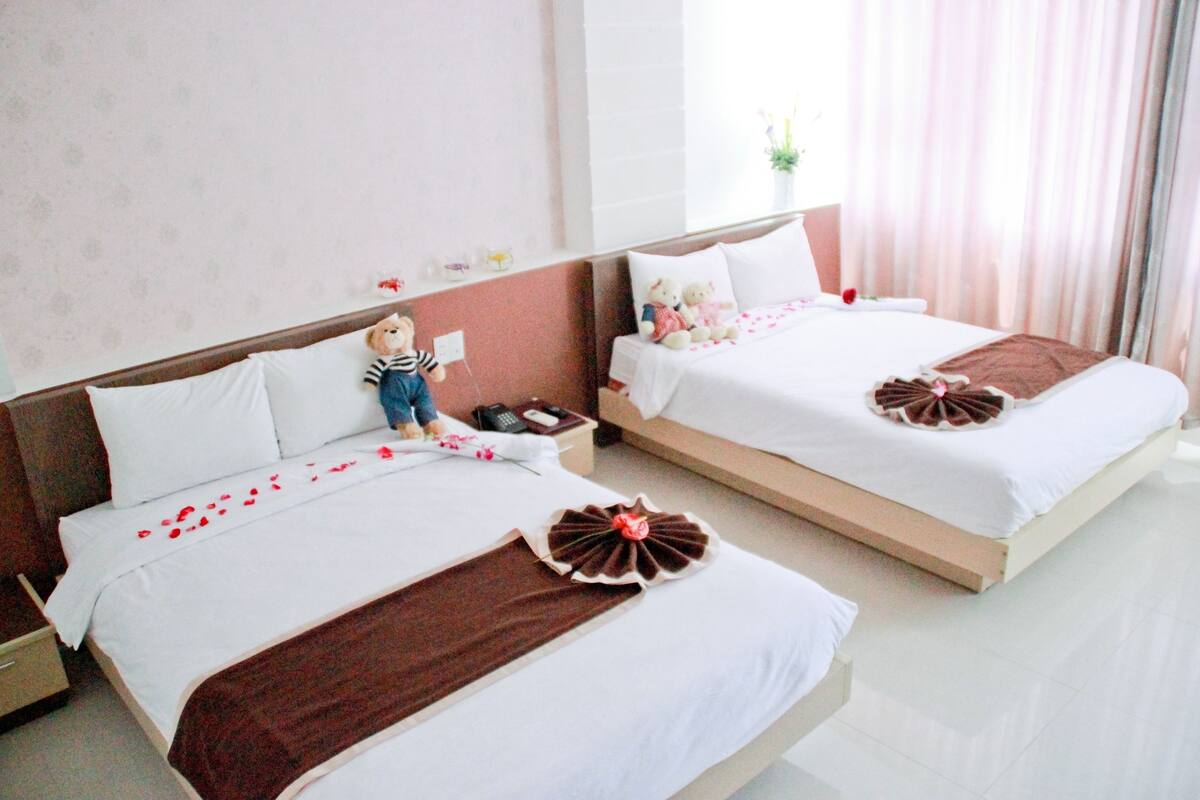 A hotel room with two beds, each with a decorative pillow and a small bedside table with a phone.