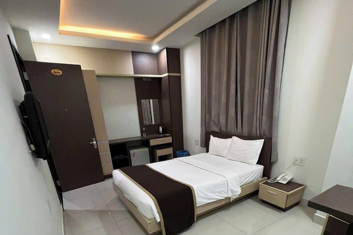 A modern hotel room with a bed, bedside table, and a desk with a chair.
