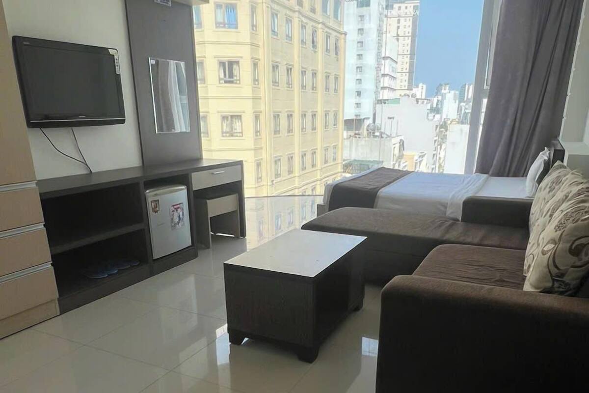 A modern living room with a sofa set, a coffee table, a flat-screen TV mounted on the wall, and a small refrigerator.