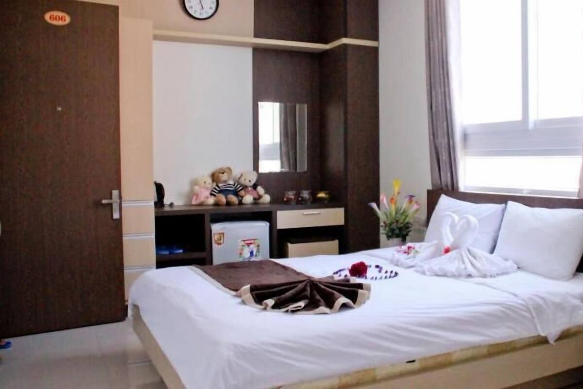 A hotel room with a bed, bedside table, a clock, a dresser, a mirror, and a window with curtains.
