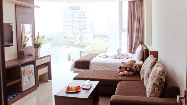 A hotel room with a bed, a sofa, a TV, a desk, and a view of the city. - Princess Hotel (Da Nang)