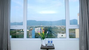 A room with a large window, a small table with a vase of flowers, and two bottles of water. - Princess Hotel (Da Nang)