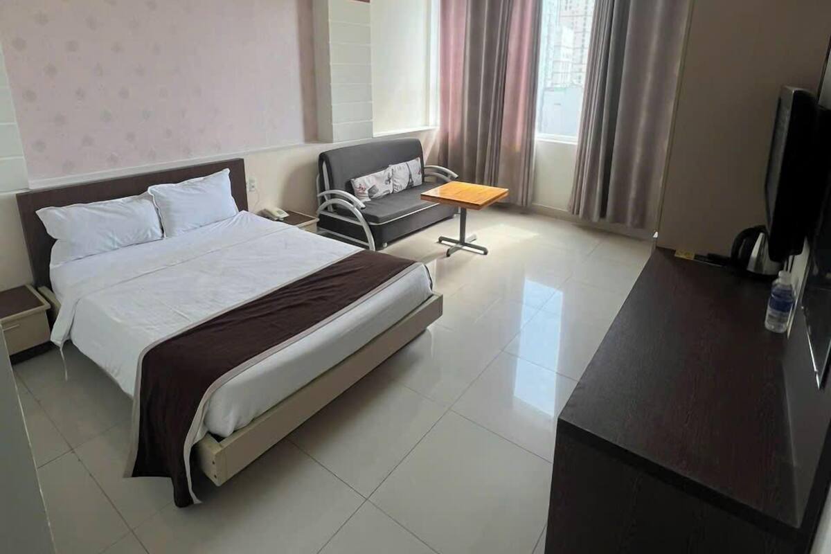 A hotel room with a bed, bedside table, desk, chair, and a TV.