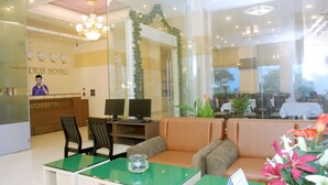 A hotel reception area with a reception desk, two computer monitors, a green table, and a sofa. - Princess Hotel (Da Nang)