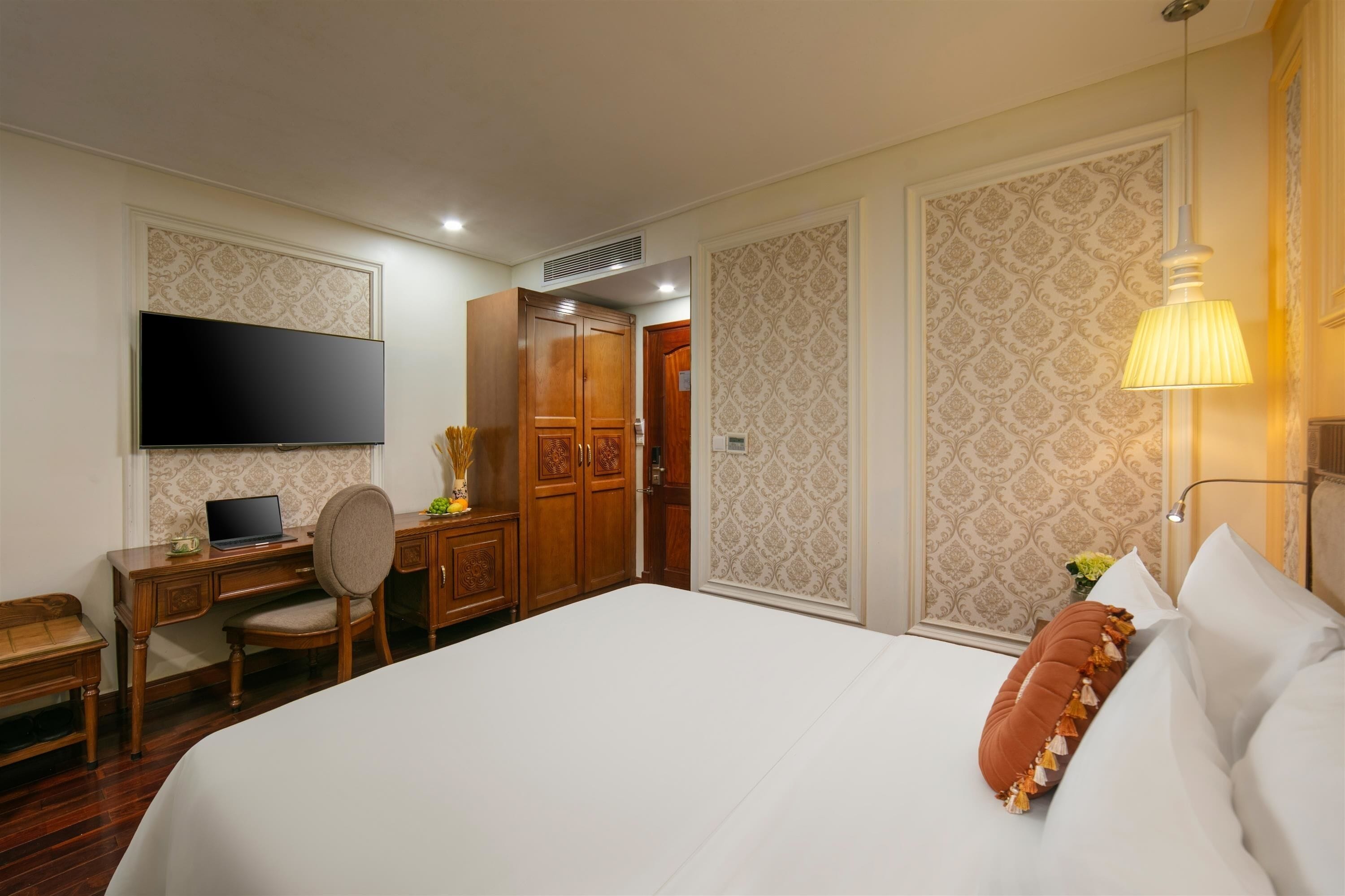 A hotel room with a large bed, a desk with a laptop, a television, and a wardrobe.