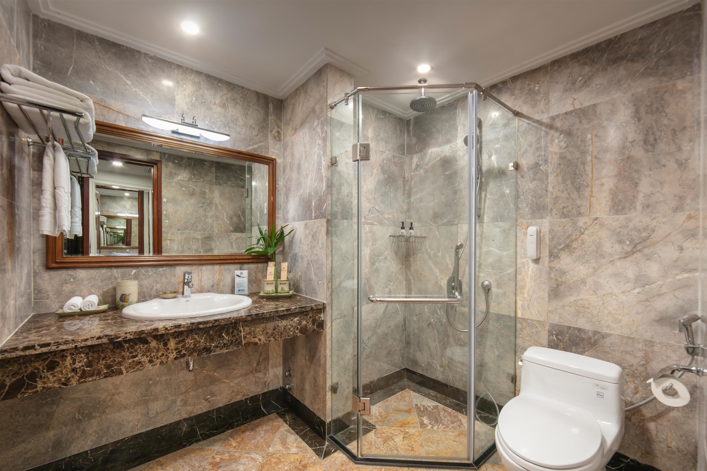 A modern bathroom with a glass-enclosed shower, a marble-tiled floor, a sink with a marble countertop, and a toilet.