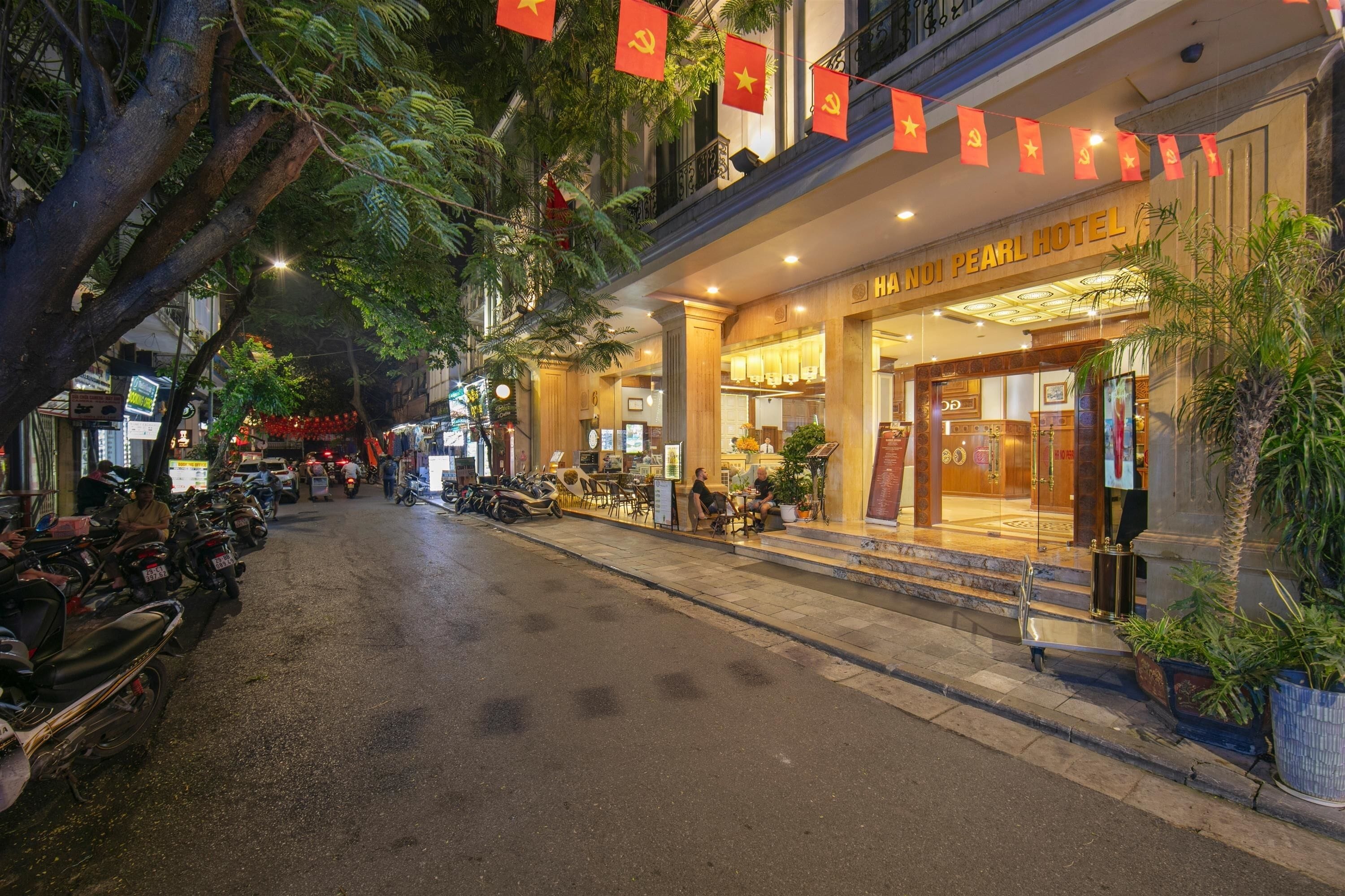 A hotel entrance with a sign reading "HANUI PEARL HOTEL," a covered outdoor seating area, and a street with parked motorcycles.