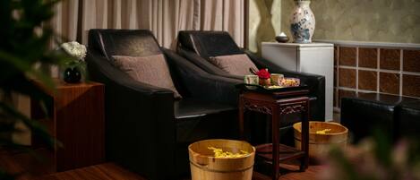 A room with two black leather sofas, a small wooden table, a vase with pink flowers, and a wooden bucket on the floor.