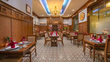 A hotel dining area with multiple tables set for dining, a chandelier, and patterned floor tiles.