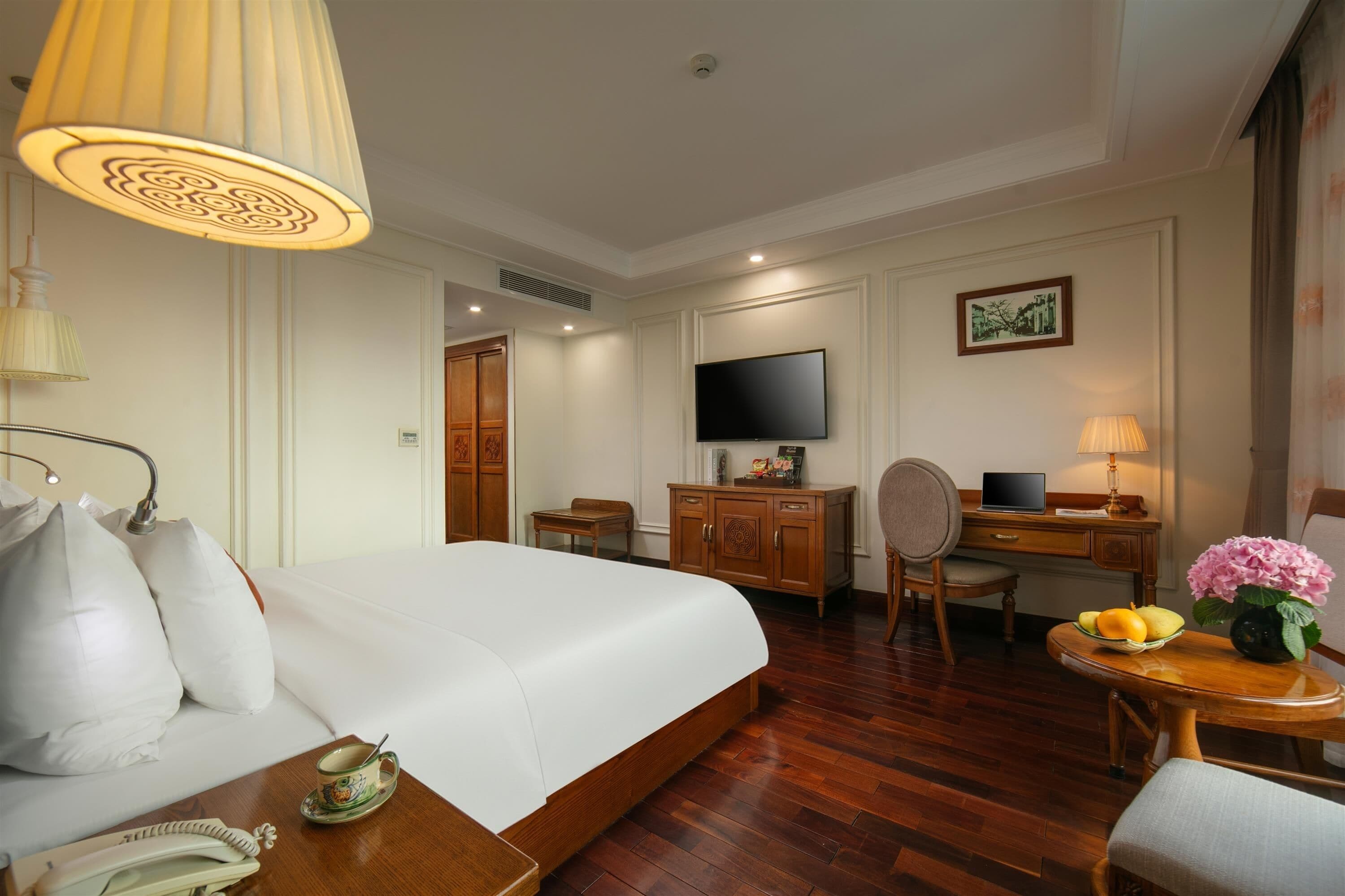 A hotel room with a large bed, a desk with a computer, a television, and a dining area with a table and chairs.