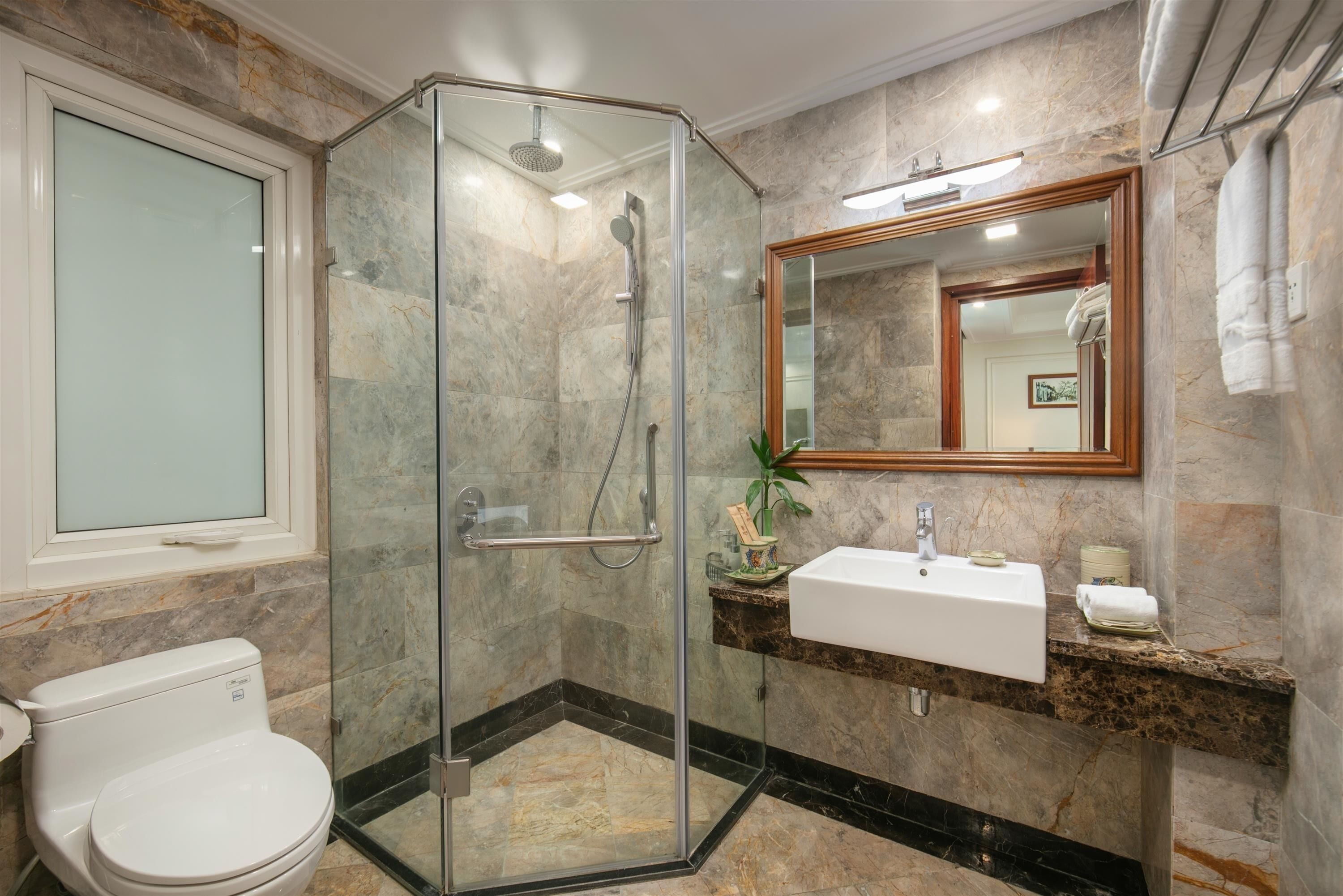 Une salle de bain moderne avec une douche en verre, un lavabo blanc et un mur recouvert de carreaux de marbre.