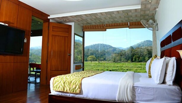 A bedroom with a large bed, wooden wardrobe, and a TV. - Hotel Tigers Roare' (Peermade)