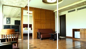 A room with a wooden floor, a sofa, a small table, and a cabinet. - Hotel Tigers Roare' (Peermade)
