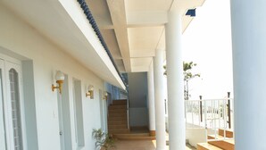 A covered corridor with white columns, a wooden floor, and a staircase leading to an upper level. - Sealine Beach Resort (Kochi)