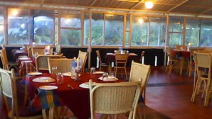 A restaurant with wooden tables and chairs, large windows, and a ceiling fan. - Sealine Beach Resort (Kochi)
