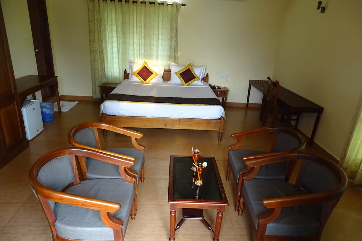 A hotel room with a bed, two wooden chairs, a small table with a drink, and a nightstand with a phone.