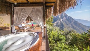 Un jacuzzi con vista a la montaña, techo de paja y zona de piscina con sillas de descanso.