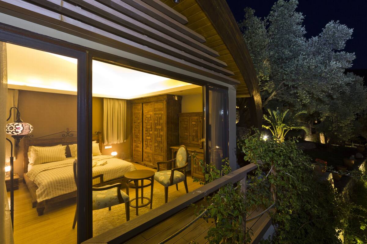 A bedroom with a large bed, a sitting area with a table and chairs, and a view of the outdoors.