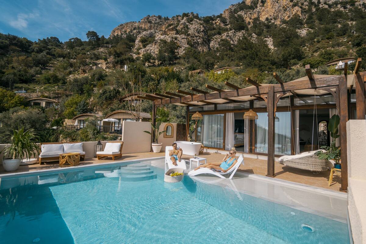 A pool area with lounge chairs and a pergola, surrounded by a mountainous landscape.
