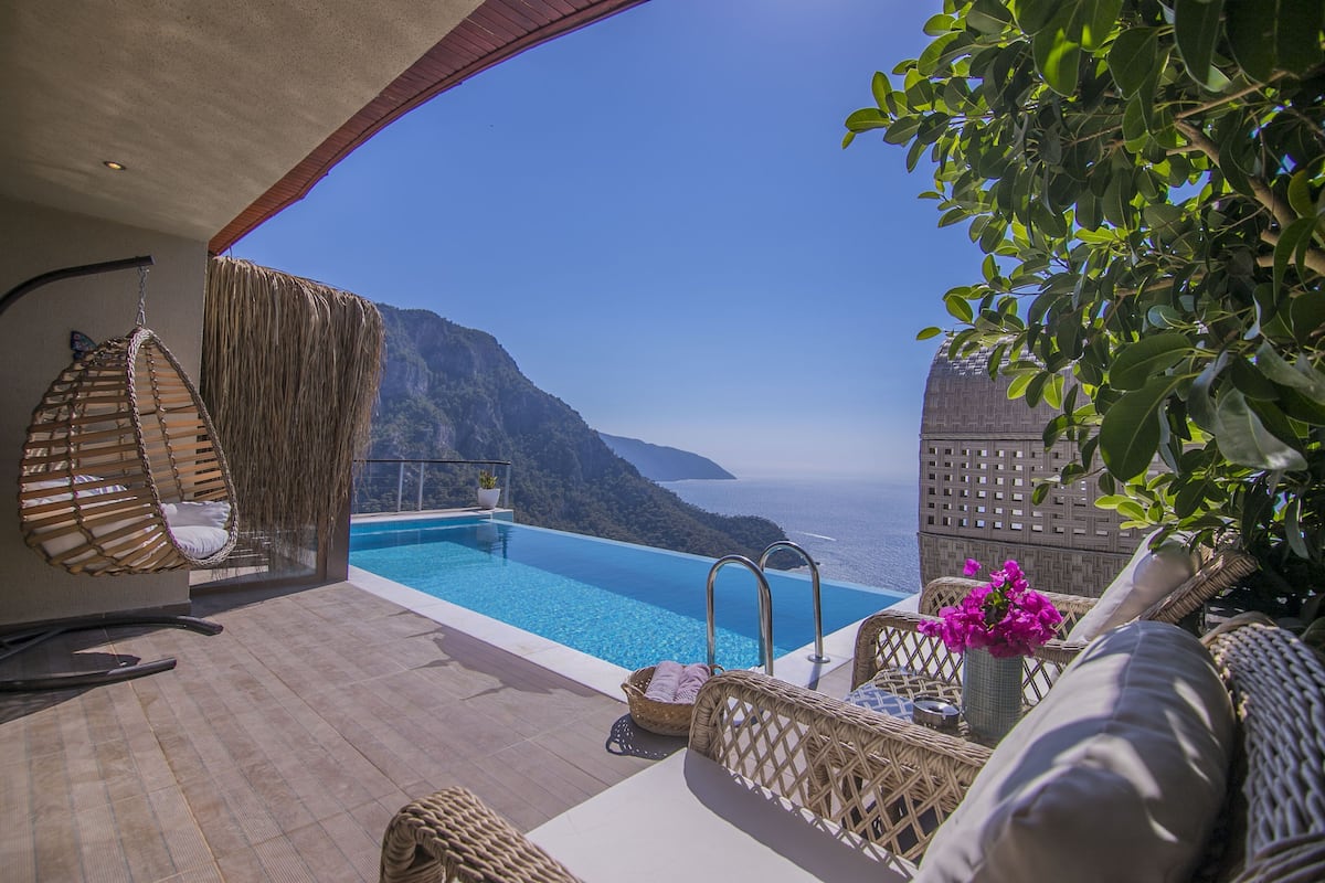 A poolside area with wicker furniture, a hanging chair, and a view of the sea.