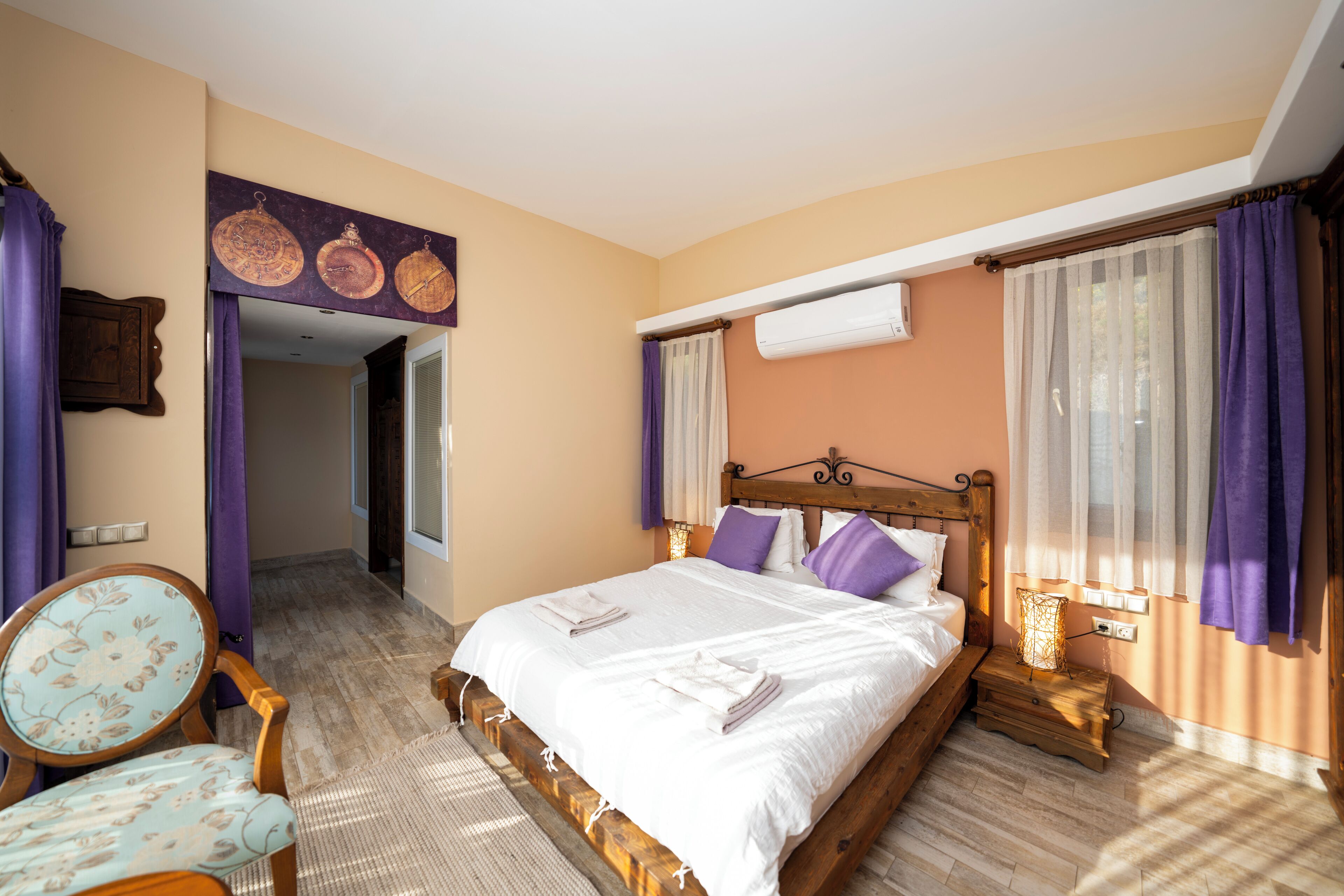 A bedroom with a wooden bed, a chair, a nightstand, and a wall-mounted air conditioning unit.