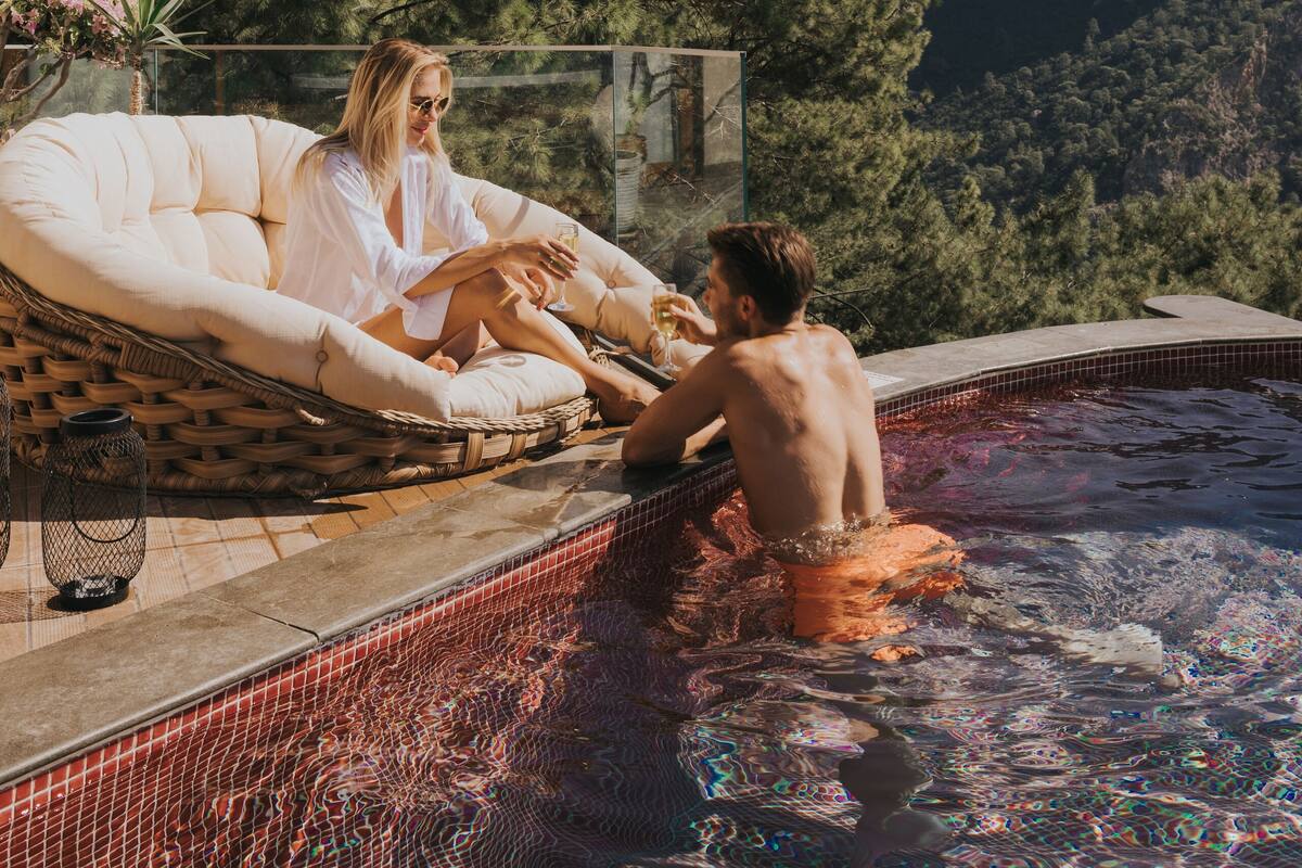 A pool area with a hot tub, lounge chairs, and a view of a mountainous landscape.