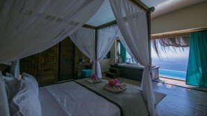 Un dormitorio con una cama grande, una mesita pequeña y vista al océano.