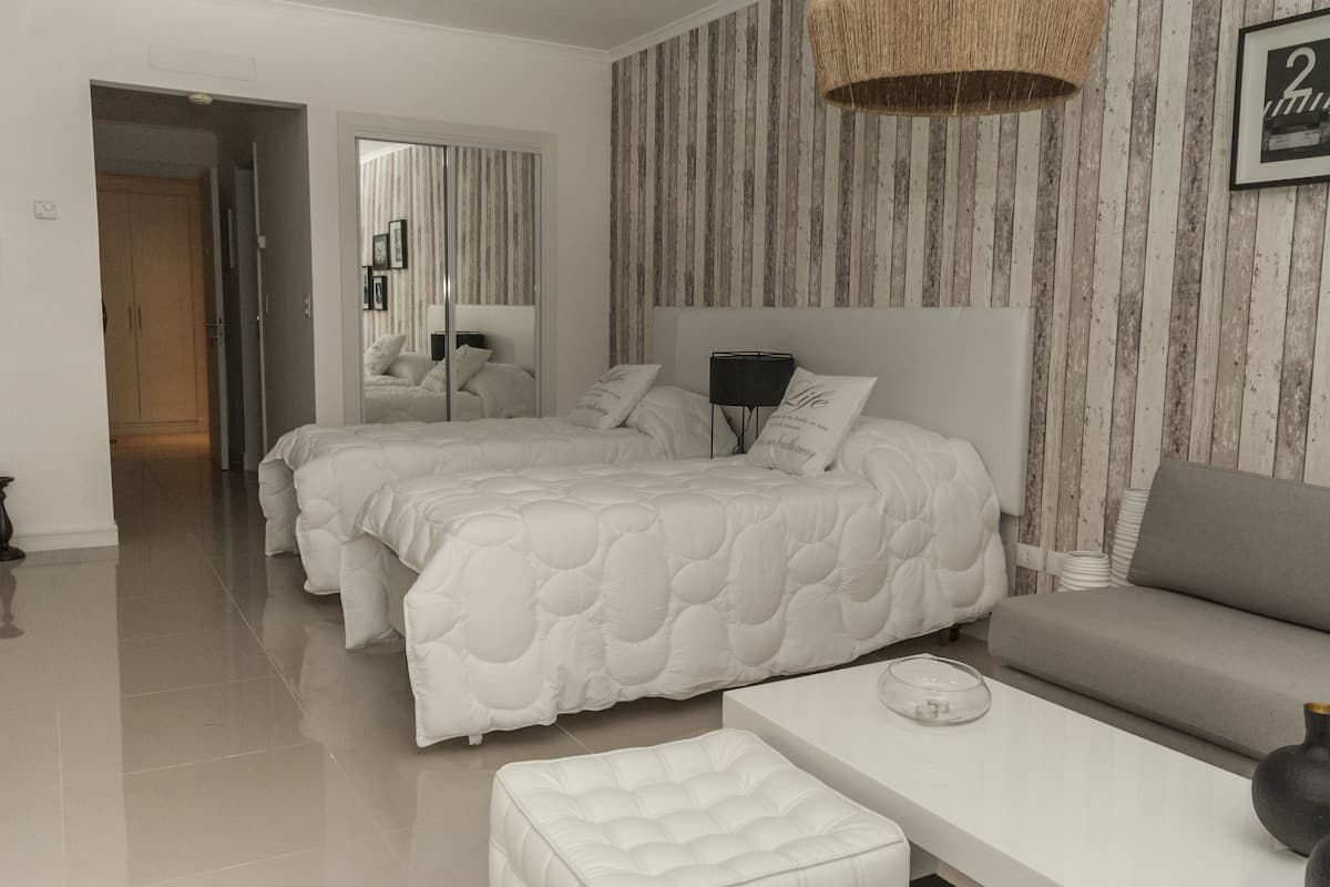 A hotel room with two beds, a sofa, a bedside table, and a mirror.