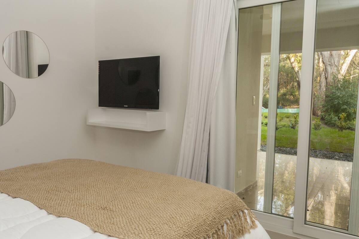 A bedroom with a bed, a mounted TV, and a sliding glass door leading to a garden.