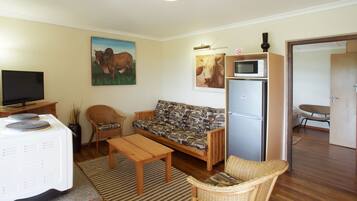 A living room with a sofa, chairs, a television, a microwave, and a refrigerator.