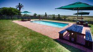 Patio trasero con piscina, mesas de picnic y sombrillas.
