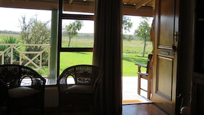 Una habitación con un ventanal grande, sillas de mimbre y una puerta con la leyenda 'Volstruis'.