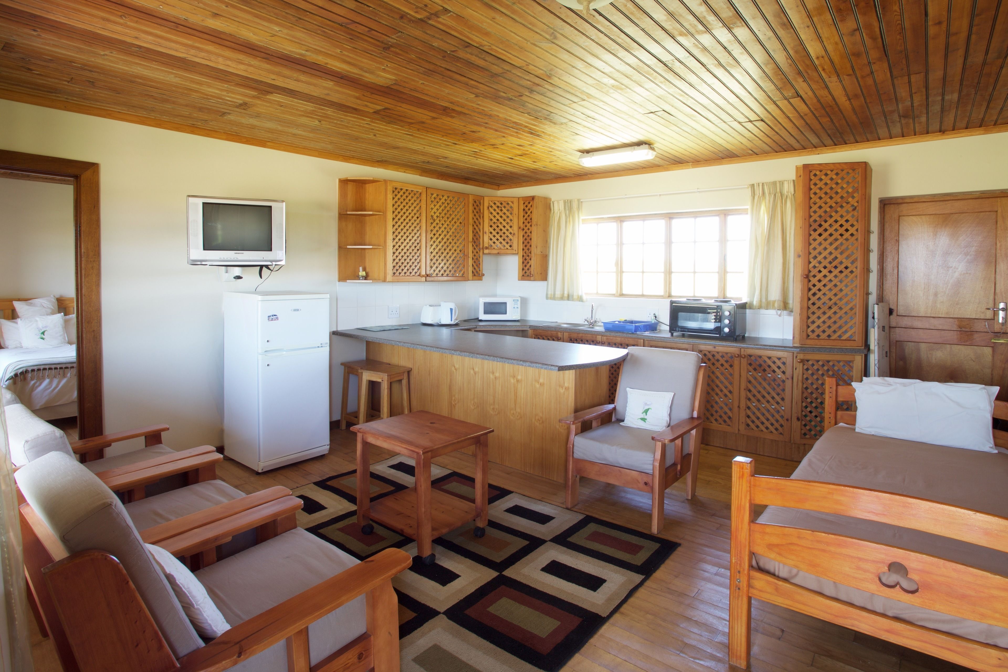 Cocina compacta con refrigerador, microondas y tostadora. Cuenta con una mesa de comedor de madera y sillas, una pequeña isla con pileta, y un televisor montado en la pared.