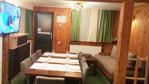 A cozy room with a wooden interior, a dining table set with chairs, a sofa, and a television on the wall. - Traveland Butique Resort Poiana Brasov (Brasov)