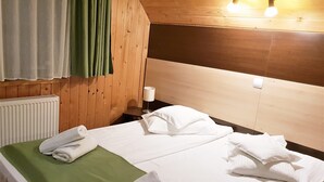 A hotel room with a wooden headboard, two beds with white linens, a green throw blanket, and a radiator. - Traveland Butique Resort Poiana Brasov (Brasov)
