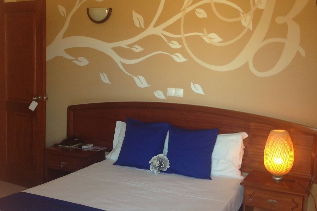 Ein Schlafzimmer mit einem Bett, einem Nachttisch, einer Lampe und einer Wand mit floralem Dekor.