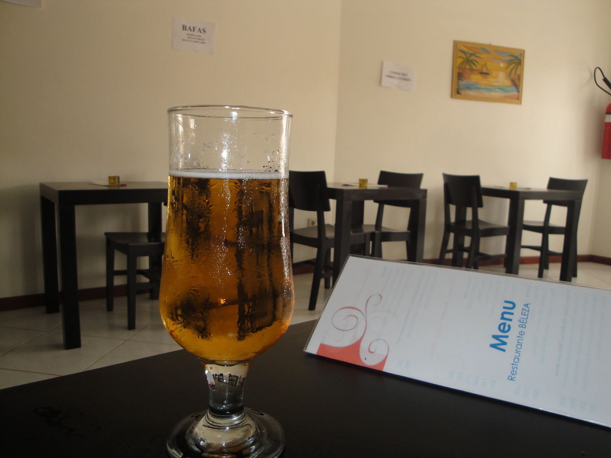 Ein Bierglas auf einem Tisch, davor eine Speisekarte, in einem Raum mit Tischen und Stühlen.
