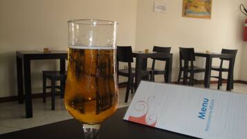 Ein Bierglas auf einem Tisch, davor eine Speisekarte, in einem Raum mit Tischen und Stühlen.