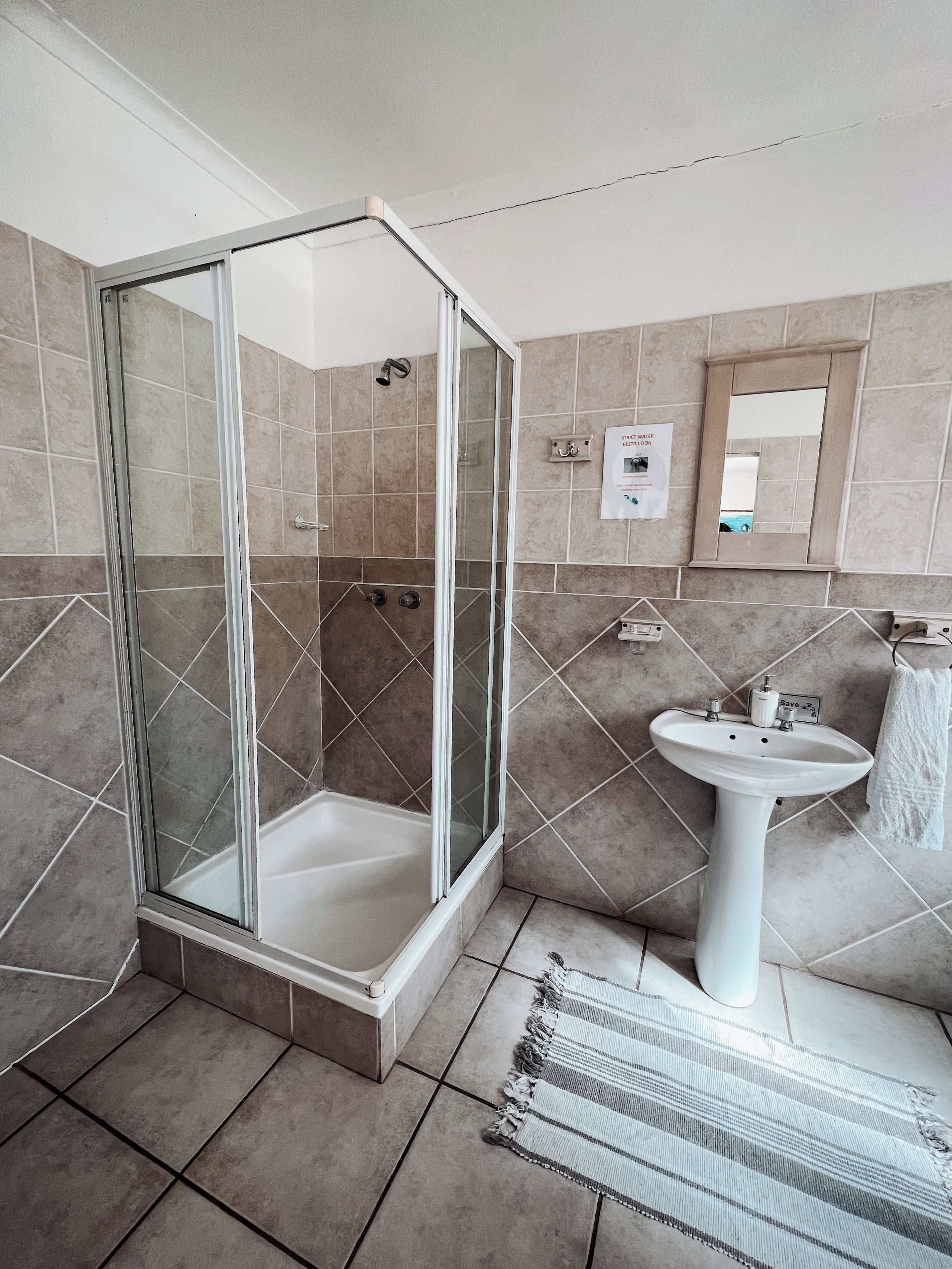 A bathroom with a glass-enclosed shower, a pedestal sink, and a tiled floor.
