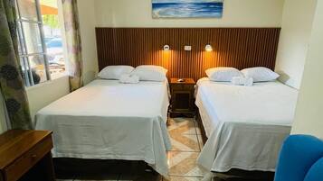 Une chambre d’hôtel avec deux lits, une chaise bleue, une table de chevet en bois, un tableau au mur et une fenêtre avec des rideaux.