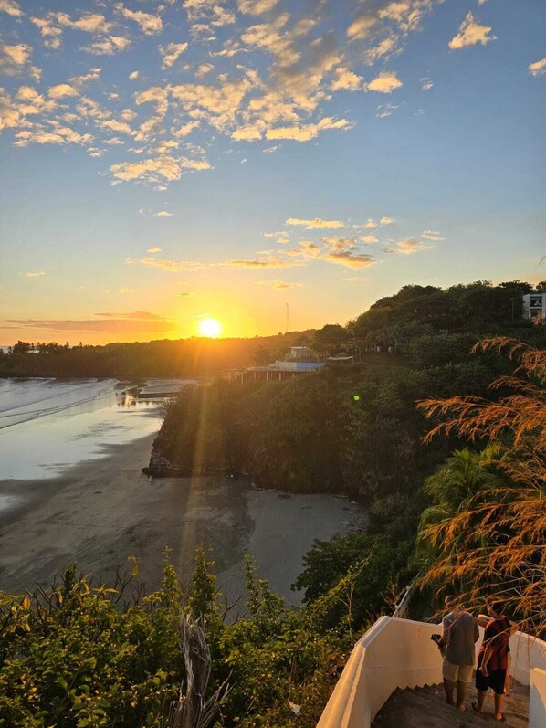 Paisaje costero con un atardecer, playa y vegetación.