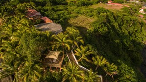 An aerial view of a resort with palm trees, a small building with a red roof, and a staircase leading up.